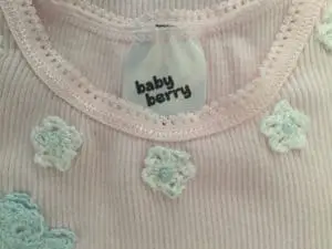 Crochet flowers on a baby singlet, closeup